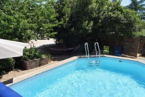 Ein rechteckiger Pool mit einer Leiter, umgeben von Bäumen und einem Holzzaun.