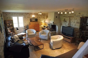 A cozy living room with a fireplace, a television, and a stone wall.