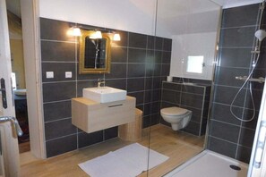 Ein modernes Badezimmer mit einer Duschkabine aus Glas, einem weißen Waschbecken mit goldener Spiegelrahmung und einer Toilette.