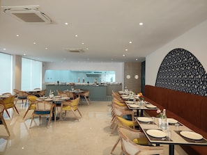Un restaurant avec une longue table à manger, des chaises et une cuisine en arrière-plan.