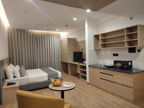 Une chambre d’hôtel moderne équipée d’un lit, d’une petite table ronde avec un panier de fruits, d’un canapé et d’une kitchenette avec un four à micro-ondes.
