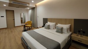 Moderni hotellihuone, jossa on suuri sänky, yöpöydät, työpöytä tuolilla ja kattotuuletin.