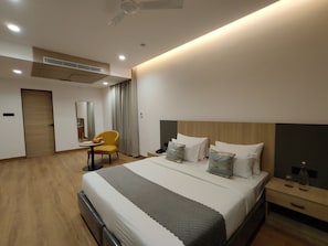 Une chambre d’hôtel moderne avec un grand lit, des tables de chevet, un bureau avec une chaise et un ventilateur de plafond.