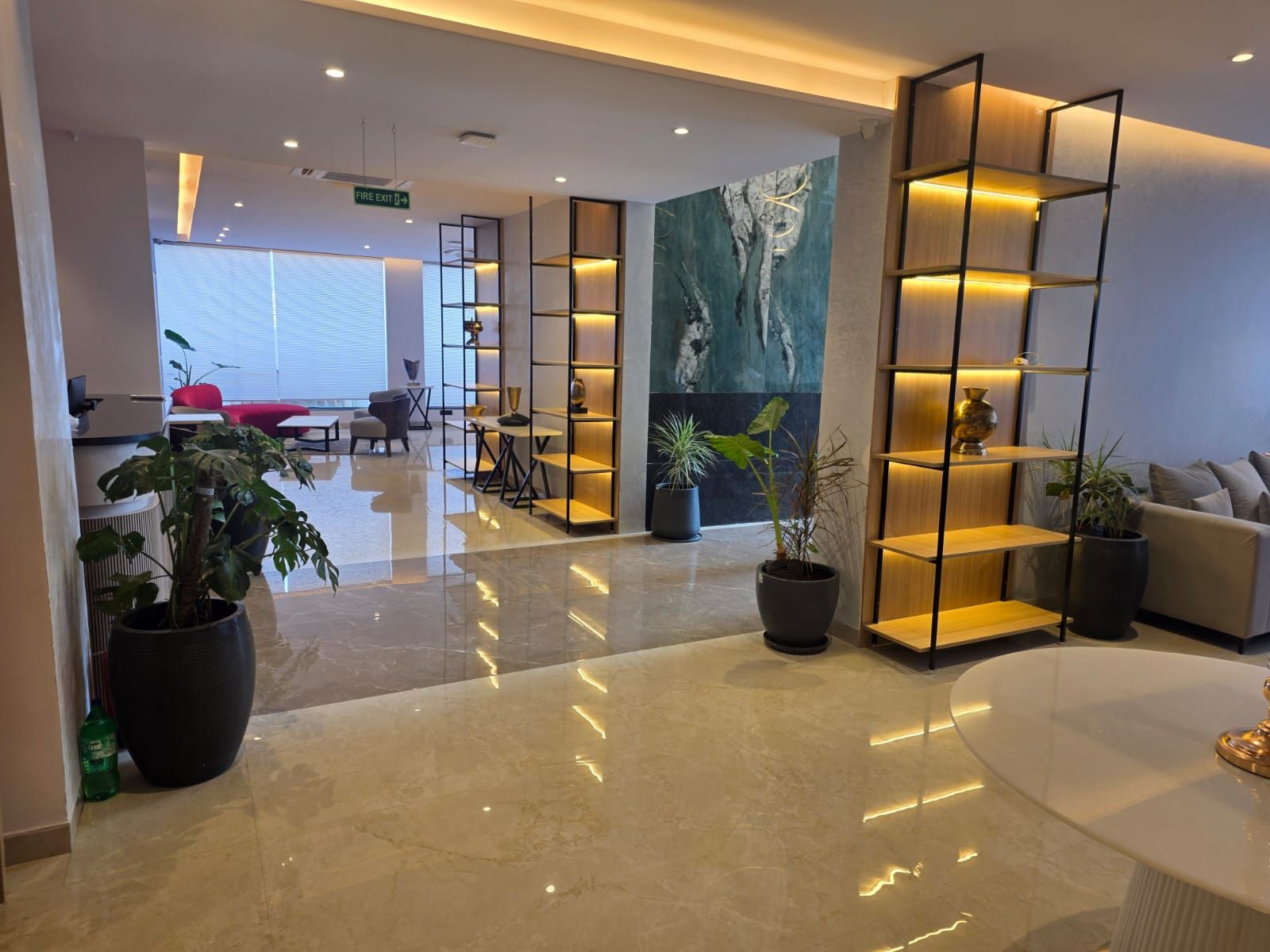 A modern lobby with a marble floor, potted plants, a reception desk, and a seating area with a sofa and chairs.