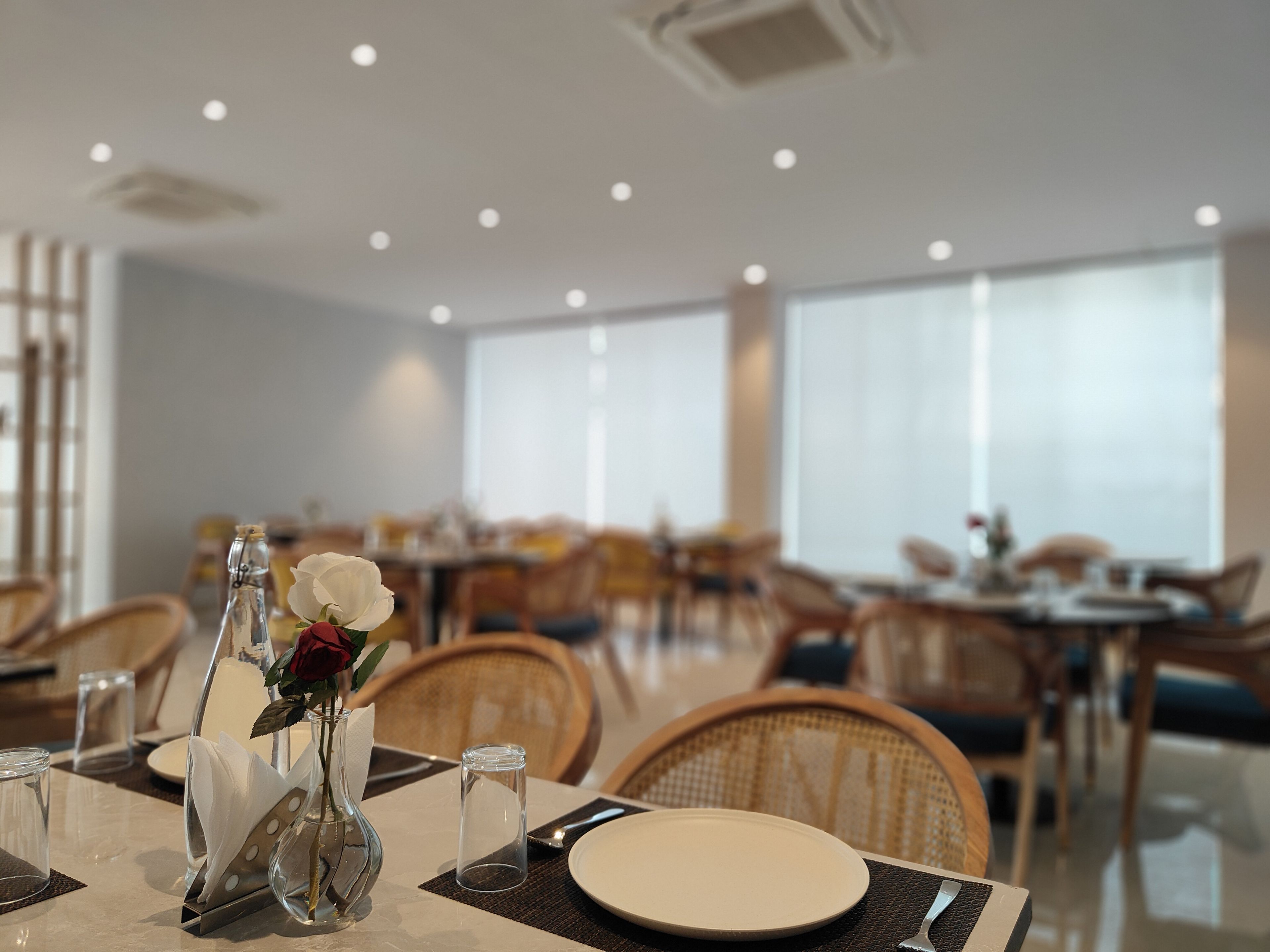 A dining area with tables set for service, chairs, and a vase with a flower on the table.