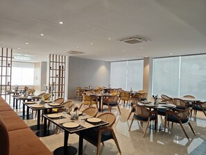 Un comedor moderno con varias mesas y sillas, un ventanal con persianas y un separador decorativo.