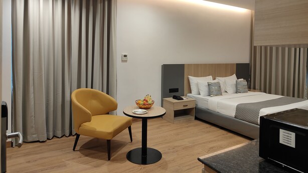 Hotellihuone, jossa on sänky, yöpöytä, tuoli, pieni pyöreä pöytä, jonka päällä on hedelmäkulho, sekä seinässä oleva ohjauspaneeli.