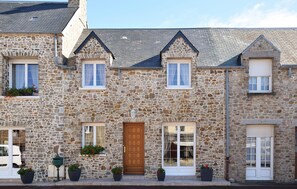 A stone building with a wooden door, multiple windows, and potted plants. - 3 bedroom cozy home in Creances (Creances)