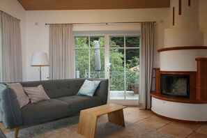 A living room with a sofa, a small wooden table, a fireplace, and a sliding glass door leading to a balcony. - Holiday home in Andechs with swimming pool (Andechs)