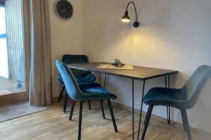 Uma sala de jantar com uma mesa de madeira, duas cadeiras azuis, um relógio de parede e um abajur.