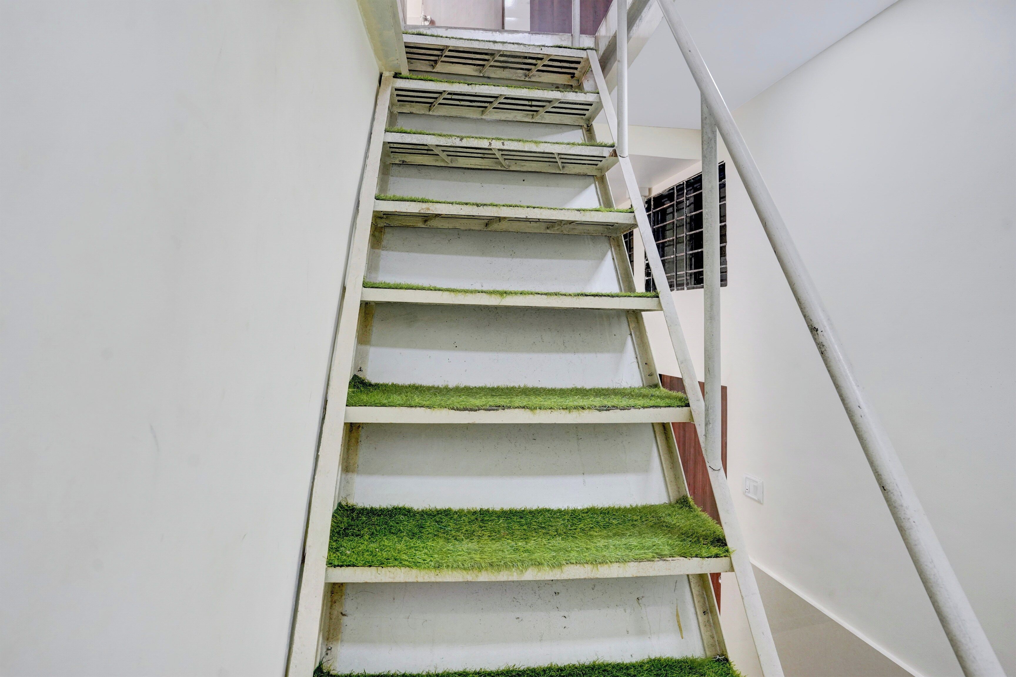 A staircase with white walls and green artificial grass steps.