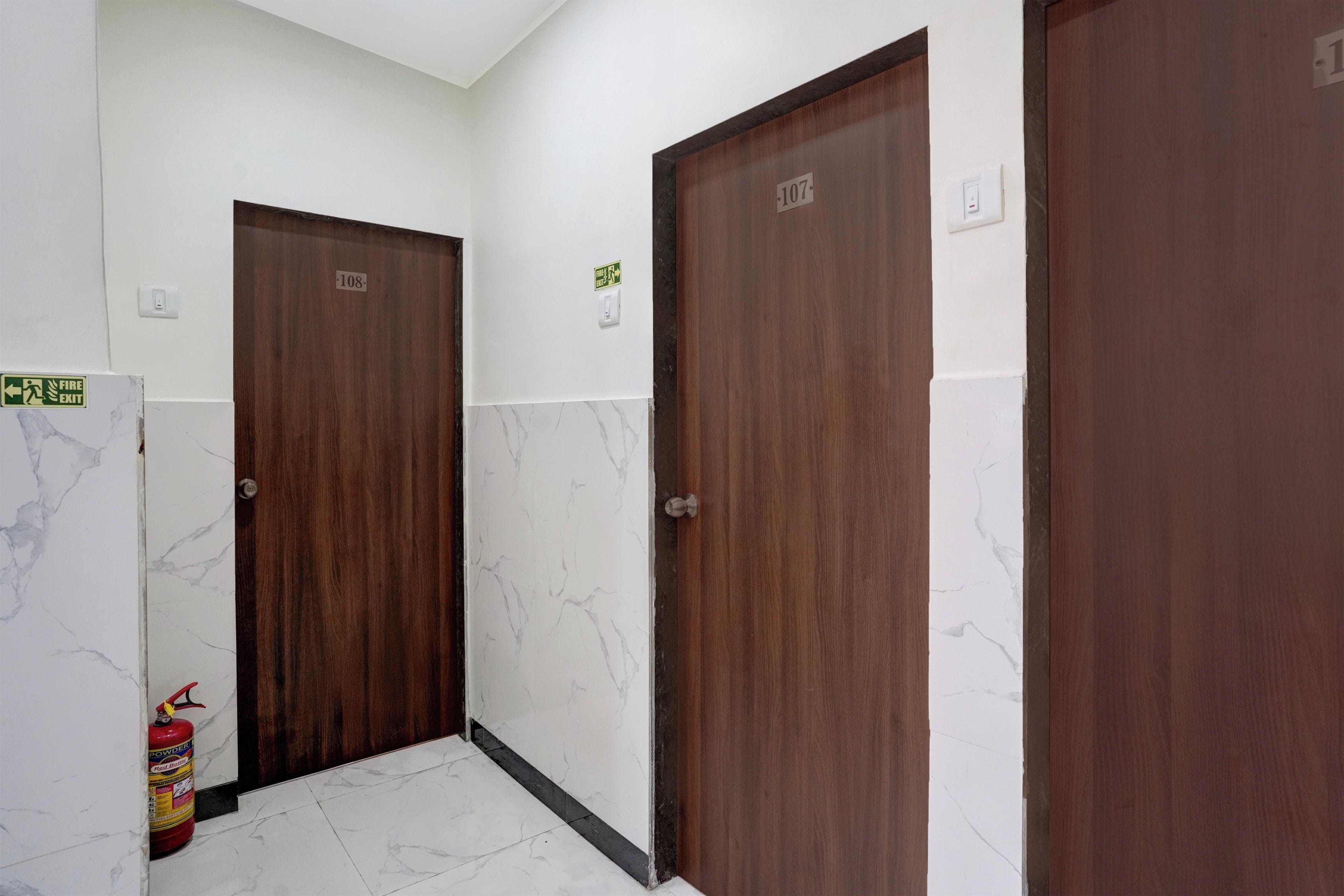 Un pasillo con dos puertas de madera, cada una con un número. Hay un extintor en la pared de la izquierda.