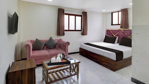 Una habitación de hotel compacta con una cama, un sofá, una mesa de centro y una mesita de noche de madera.