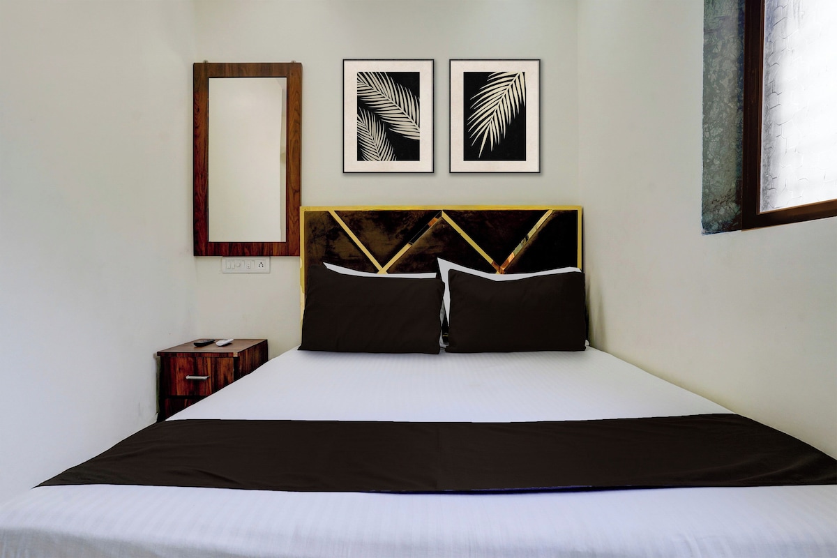 Une chambre d’hôtel avec un lit, une table de chevet, un miroir et deux motifs de feuilles encadrés accrochés au mur.