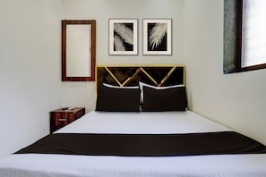 Une chambre d’hôtel avec un lit, une table de chevet, un miroir et deux motifs de feuilles encadrés accrochés au mur.