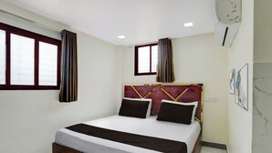 Una habitación de hotel con cama, cortinas, una ventana y un aire acondicionado de pared.