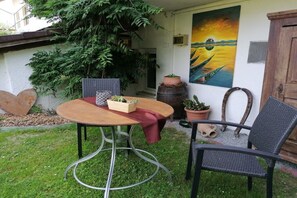 A patio with a round table, two chairs, potted plants, and a painting on the wall. - Dreisessel - Neukirchinger Holiday Farm (Tiefenbach)