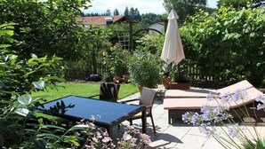 Um pátio externo com mesa, cadeiras, área de estar e uma pérgola com guarda-sol.