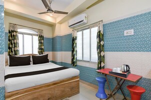 Habitación de hotel con una cama, un escritorio, una silla roja, un inodoro azul y un equipo de aire acondicionado.