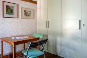 Ein Zimmer mit einem Holztisch, zwei Stühlen, einem weißen Schrank und zwei gerahmten Bildern an der Wand.