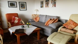 A living room with a grey sofa, a wooden coffee table, a red and white patterned armchair, and a beige armchair. - Holiday apartment in Polle with swimming pool (Polle)