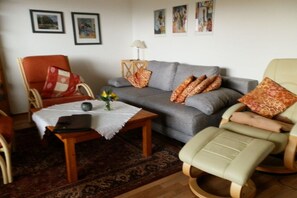 A living room with a grey sofa, a wooden coffee table, a red and white patterned armchair, and a beige armchair. - Holiday apartment in Polle with swimming pool (Polle)