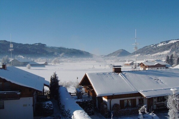Vila coberta de neve com casas de madeira tradicionais, céu claro e montanhas ao longe.