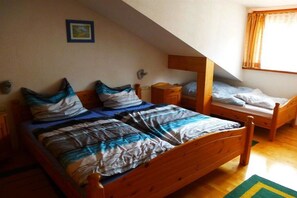 Quarto com duas camas de madeira, mesa de cabeceira, cômoda e janela com cortinas.