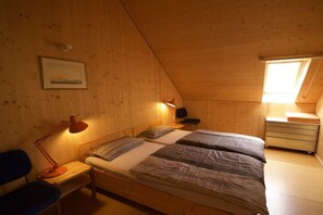 A cozy room with a sloped ceiling, two beds with striped bedding, a desk with a lamp, a chair, and a small bedside table. - Basseltang Hus - S"Denn (Todtnau)