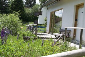 A rustic building with a wooden deck, surrounded by lush greenery and wildflowers. - Basseltang Hus - S"Denn (Todtnau)