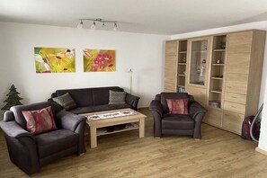 Uma sala de estar com sofá, duas poltronas, mesa de centro e aparador de madeira.