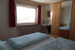 Quarto com duas camas, janela com cortinas, radiador, pia e armário.