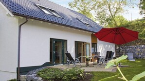 Una casa moderna con techo inclinado, un patio con mobiliario exterior y un paraguas rojo.