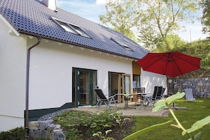 Ein modernes Haus mit geneigtem Dach, einer Terrasse und Gartenmöbeln sowie einem roten Sonnenschirm.
