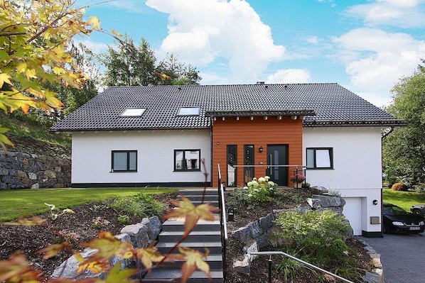 Ein modernes, zweistöckiges Haus mit Ziegeldach, einer Holztür und einem kleinen Balkon.