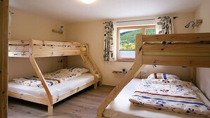 Una habitación con literas, una ventana con cortinas, una mesita y una lámpara de pared.