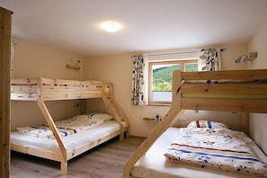 Ein Zimmer mit Etagenbetten, einem Vorhangfenster, einem kleinen Tisch und einer Wandlampe.