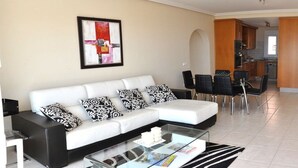 Een moderne woonkamer met een witte bank, zwart-wit gestreepte kussens, een glazen salontafel en een eethoek met zwarte stoelen.