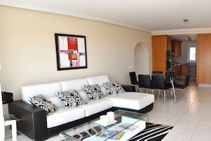A modern living room with a white sofa, black and white patterned cushions, a glass coffee table, and a dining area with black chairs. - Great views || Morro Jable, Fuerteventura (Morro Jable, Fuerteventura)