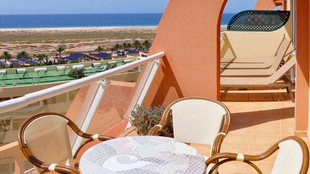 Een balkon met uitzicht op het strand, een tafel met stoelen en een parasol.