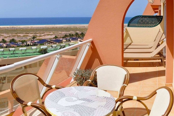 A balcony with a view of the beach, a table with chairs, and a sunshade. - Great views || Morro Jable, Fuerteventura (Morro Jable, Fuerteventura)
