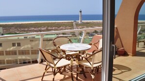 Een balkon met een tafel en stoelen, met uitzicht op een strand en een vuurtoren.