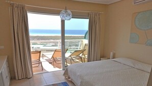 Een slaapkamer met een groot bed, uitzicht op het strand en een balkon met stoelen.