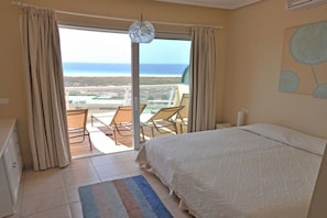 A bedroom with a large bed, a view of the beach, and a balcony with chairs. - Great views || Morro Jable, Fuerteventura (Morro Jable, Fuerteventura)