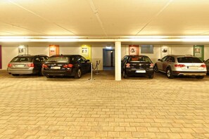 A parking garage with multiple cars parked in rows, a brick floor, and overhead lighting. - Citrine Suite ARCHDUKE GISELA (Oberstdorf)