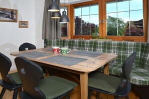A dining area with a wooden table, green upholstered chairs, a plaid bench, and a window with curtains. - Apartment with 1 bedroom (Reit im Winkl)