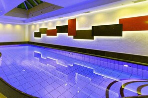 Piscina com piso ladrilhado e parede com luminárias geométricas.