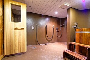 Uma sala de sauna com bancos de madeira, porta de madeira e sistema de chuveiro fixado na parede.