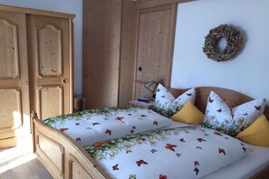 A bedroom with a wooden wardrobe, a bed with floral bedding, and a wall wreath. - Alpenflair holiday apartment 228 (Oberstdorf)