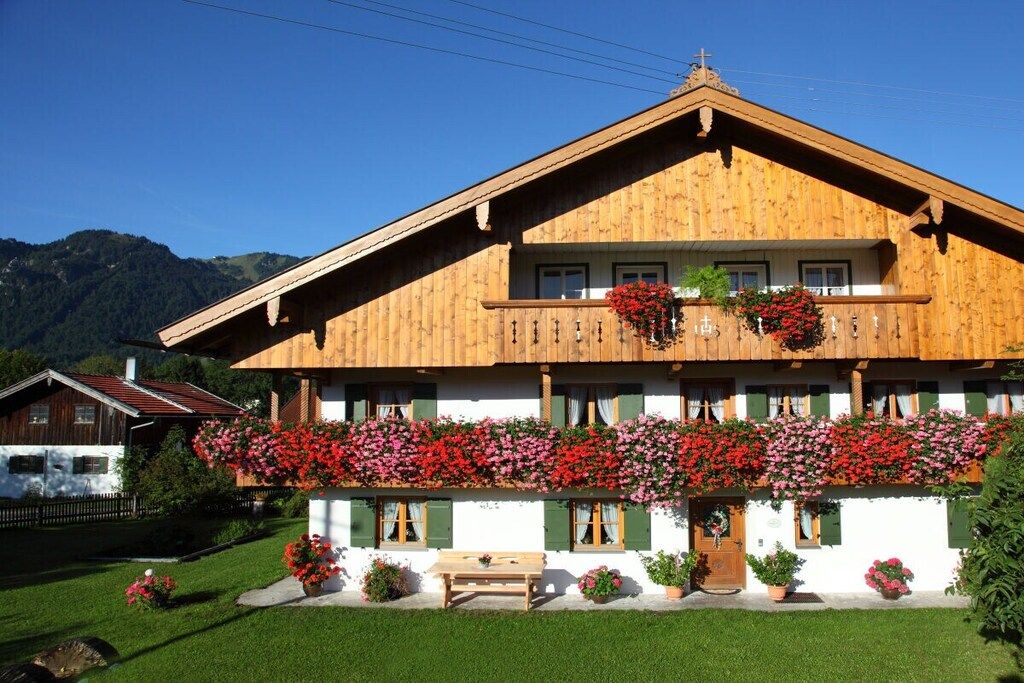A wooden chalet with a balcony, surrounded by greenery and mountains.
